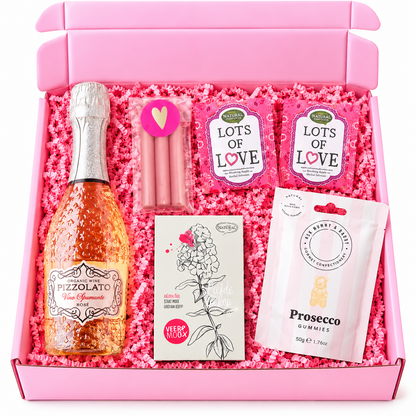 Feestelijke roze verjaardagscadeaubox met rosé bubbels, prosecco-gummies, roze kaarsjes, liefdesthee en roze opvulmateriaal.