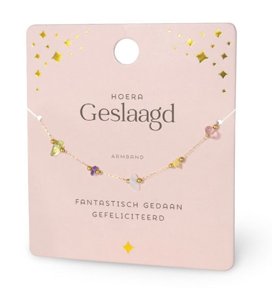 Lichtroze ‘Hoera Geslaagd’ cadeaukaart met verfijnd goudkleurig armbandje en kleurrijke edelsteentjes. Stijlvol geslaagd cadeau voor diploma of examen