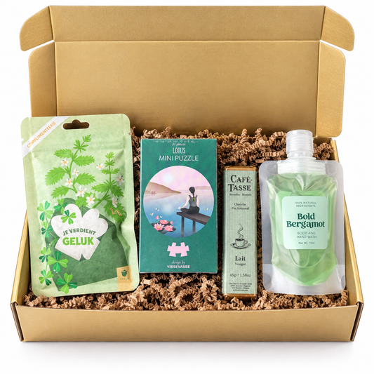 Cadeaubox in gouden kraftdoos met groene geluksattentie, mini puzzel, Café-Tasse melkchocolade met nougat en Bold Bergamot body- en handwash, gevuld met bruine papiersnippers.