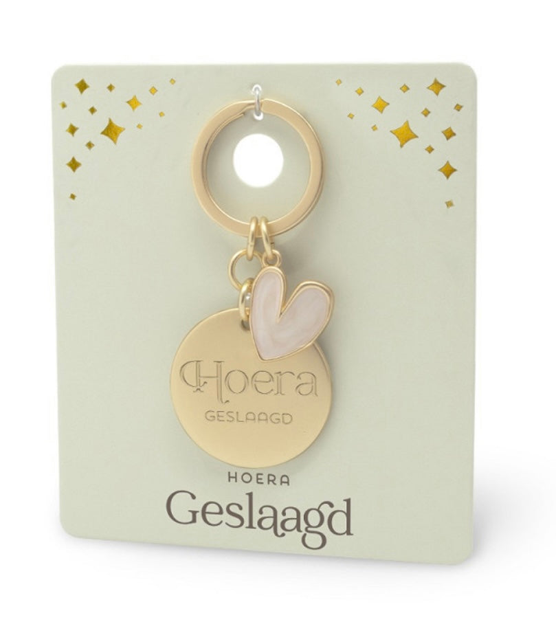 Goudkleurige ‘Hoera Geslaagd’ sleutelhanger met ronde hanger en lichtroze hartvormige edelsteen hanger op luxe cadeaukaart