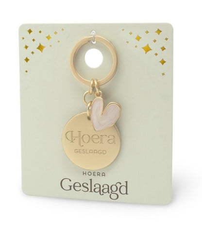 Goudkleurige ‘Hoera Geslaagd’ sleutelhanger met ronde hanger en lichtroze hartvormige edelsteen hanger op luxe cadeaukaart
