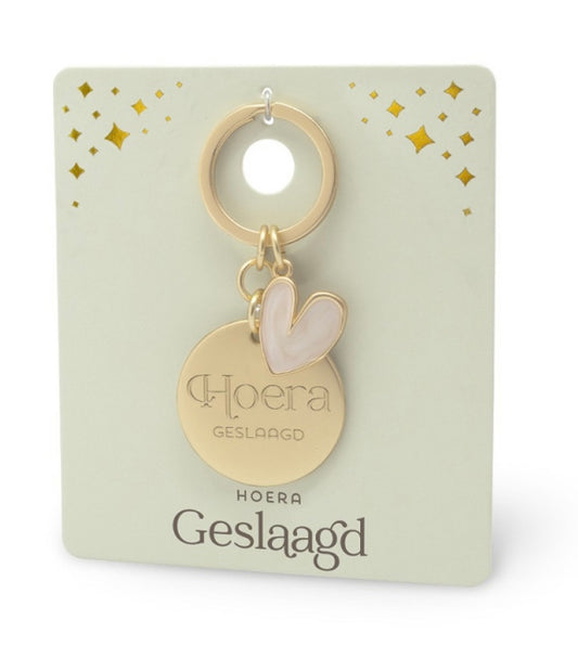Goudkleurige ‘Hoera Geslaagd’ sleutelhanger met ronde hanger en lichtroze hartvormige edelsteen hanger op luxe cadeaukaart