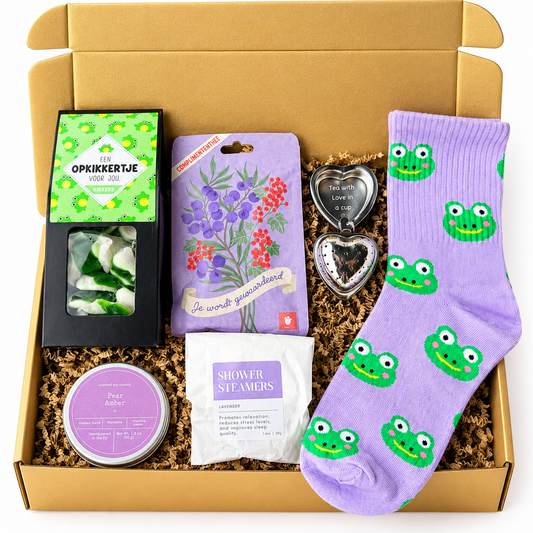 Luxe gouden cadeaubox met paarse sokken met groene kikkerprint, opkikkertje snoepjes, complimententhee, hartvormige theezeef, geurkaars en lavendel shower steamers op een witte achtergrond.