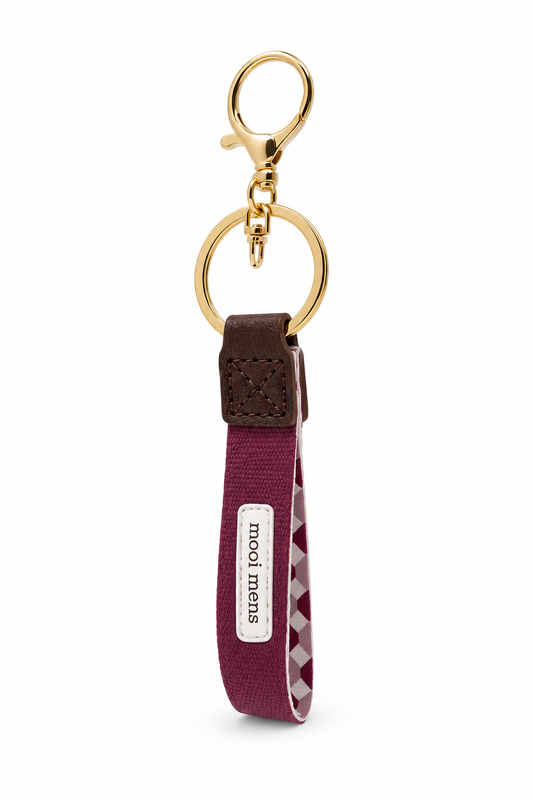 Bordeauxrode sleutelhanger met de tekst Mooi Mens, goudkleurige metalen sleutelring en elegante details.